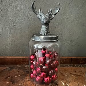 Glasbehälter mit schwarzem Rehkopf-Deckel, gefüllt mit roten Christbaumkugeln. Rustikaler Charme.