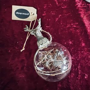 Glaskugel mit dekorativen Zweigen und einem silbernen Aufsatz, an einem braunen Etikett befestigt.