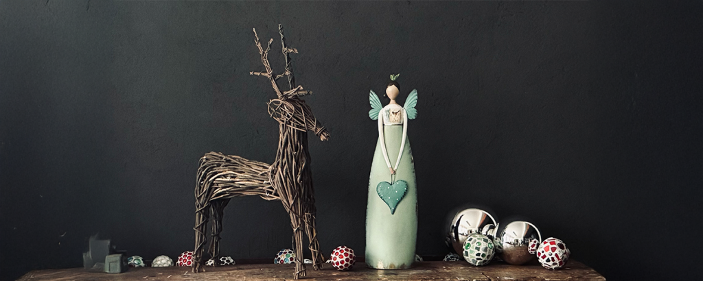 Holzdeko in Form eines Rehs und einer Engel-Figur in mintgrün, umgeben von bunten Weihnachtskugeln auf einem Holzbrett.